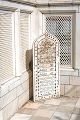 Khuldabad, MH, India, Dec 12: An arched marble inscription plaque with Persian or Urdu calligraphy and red floral motifs, set on a tiled floor against a white marble wall with jali screens.