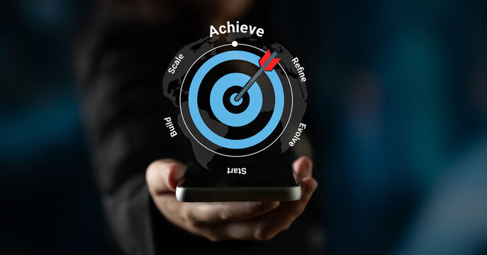 A hand presents a smartphone with a visual of a target and an arrow hitting the center, representing motivation for achieving goals and successful outcomes in business and personal growth. Gantry