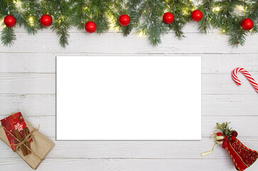 Christmas flat lay workspace with pine branches red ornaments scissors gift and white empty paper on white wooden table showing holiday crafting concept and copy space