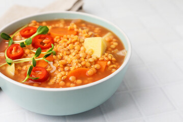 Delicious lentil soup with vegetables in bowl on white tiled table, closeup. Space for text