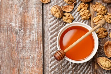 Honey in bowl, walnuts and dipper on wooden table, flat lay. Space for text