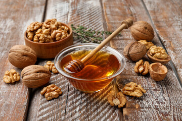 Honey in bowl, walnuts and thyme on wooden table, closeup