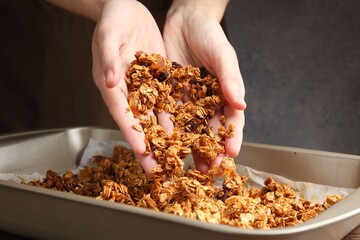 Woman putting tasty granola onto tray on table, closeup