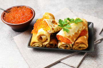 Tasty crepes with red caviar, sour cream and parsley on grey table, closeup