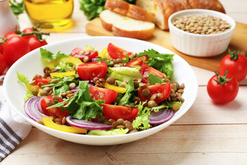 Delicious lentil salad and ingredients on light wooden table, closeup