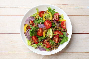 Delicious salad with lentils and vegetables on light wooden table, top view