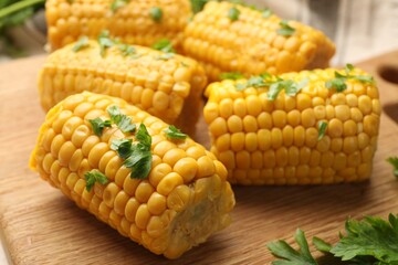 Pieces of boiled corncobs with parsley on wooden board, closeup