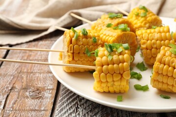 Skewers with pieces of boiled corncobs and green onion on wooden table, closeup
