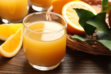 Fresh orange juice, fruits and green leaves on wooden table, closeup