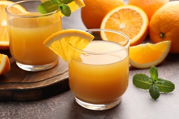 Fresh orange juice in glasses, mint and fruits on grey table, closeup