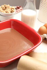 Liquid chocolate dough in baking dish, eggs, brown sugar and milk on white table, closeup