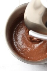 Mixing chocolate dough in bowl at white table, top view