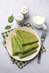 Naklejka premium Tasty spinach crepes with leaves and sour cream on grey table, flat lay