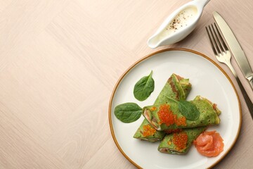 Tasty spinach crepes with salmon, avocado and red caviar served on wooden table, flat lay. Space for text