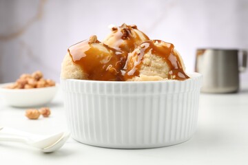 Tasty ice cream with caramel sauce and almonds on white table, closeup
