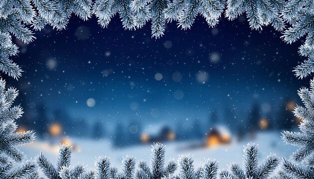 Frosted evergreen branches frame a snowy village at night with snowfall.
