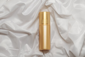 Mock up golden spray bottle for cosmetics on elegant white satin backdrop