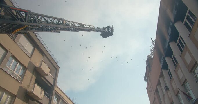 Silhouette of a fireman in a bucket on the ladder of a fire engine lifting into the air into the roof of a burning building