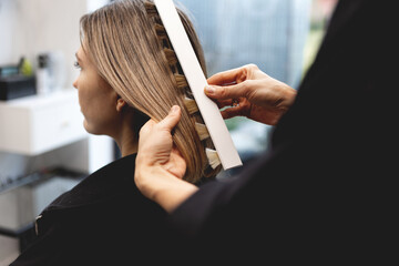 Hairdresser checking hair color of woman with professional shade chart in modern beauty salon, assessing tones and highlights with precision during color consultation