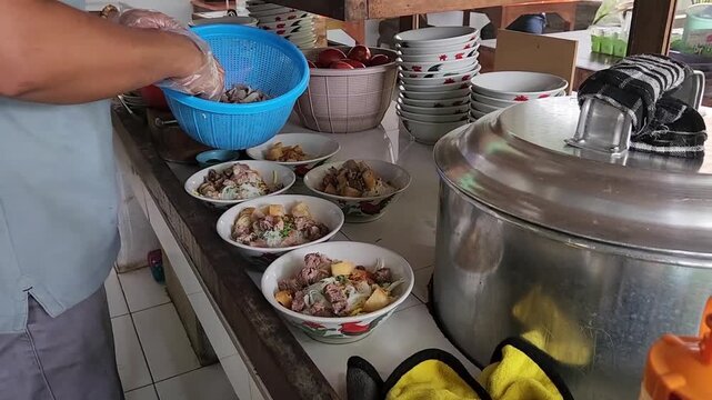 Traditional street food soto mie preparation in local kitchen. Asian noodle soup cooking process in busy food stall. Fresh beef noodle soup assembled by hand in street kitchen