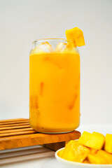 Mango smoothie in a glass stands on a wooden tray with some slice of fresh mango fruit on the foreground. Vitamin-rich and healthy eating concept.