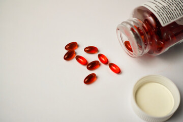 A photo of red pills spilling out from a dropped medicine container on a white table. Healthcare and medical concept