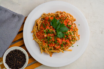 Top view of a spaghetti with tomato sauce and small dice of black pepper stand on a white textured background.