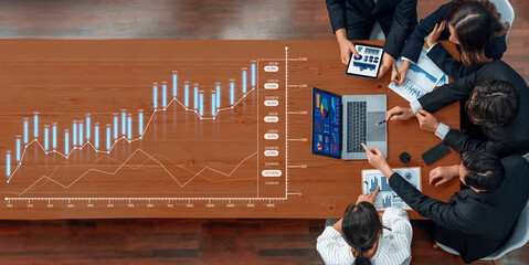 A team of business professionals engaging in a meeting to analyze financial data and market trends, using various charts and a laptop in a modern office environment. Scalp