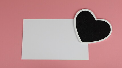 Biglietto di auguri per San Valentino con cuore nero, con cartoncino bianco per la copia su sfondo rosa.