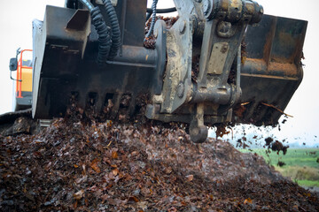 Close-up of an excavator with shredder attachment actively shredding green waste like leaves and grass. The shredder  processes organic debris for recycling, composting and fermenting