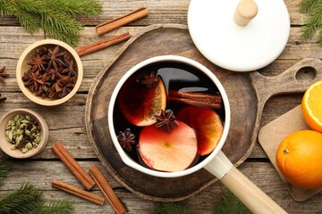 Tasty mulled wine in pot and ingredients on wooden table, flat lay