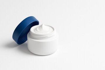 Close-up of open jar of nourishing cream or moisturizer, with dark blue cap on white background. For advertising face cream, skincare, anti-aging products and self-care. Banner with copy space