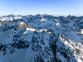 Aerial view of snow-covered mountains under clear sky with sunlight shining on peaks during daytime