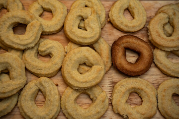 Freshly baked traditional Scandinavian Danish Christmas cookies called Vanilla rings, laying on wooden surface. One over baked black cookies sticks out, diversity and exclusion concept.