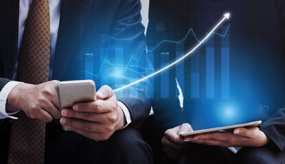 Two business professionals analyze financial data on mobile devices, surrounded by digital growth charts and indicators illustrating economic progress. Impute