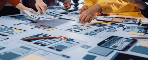 A vibrant group of creative professionals collaborates on user interface design, arranging colorful prototypes and sketches on a table, fostering innovative ideas and solutions. SACTR