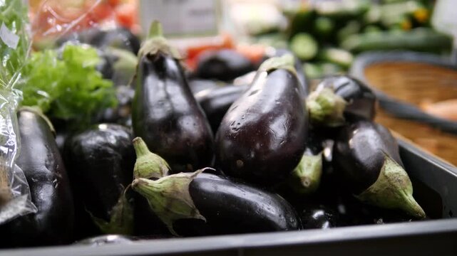 Vibrant closeup shot of a neat stack of fresh, glossy eggplants on a market stall. This video celebrates natural produce, healthy eating, and the rustic charm of local markets. 