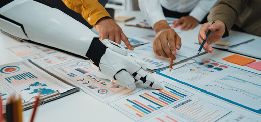 A collaborative scene showcasing human and robotic hands engaged in analyzing business charts and data in a modern office environment, highlighting innovation and teamwork.Noogenesis