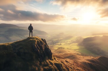 Man standing on mountain peak overlooking serene valley landscape at sunrise or sunset with cloudy sky.