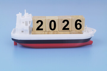 Cargo ship model with cubes with numbers 2026 on blue background. Sea ​​transportation in year 2026 concept.
