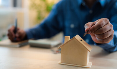 A man hand putting coins into a house bank saving bank for account save money. Planning step up,...