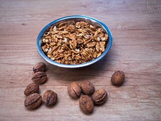 Metal bowl with raw walnut kernels and whole walnuts in shells on wooden table. Natural source of omega 3, protein and vitamins. Healthy ingredient for baking, desserts and nutritious breakfasts.