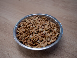 Top view of raw walnut kernels in a metal bowl on wooden table. Natural source of healthy fats, protein and vitamins. Ingredient for baking cakes, healthy breakfast, desserts and home cooking.