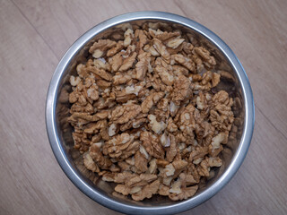 Top view of raw walnut kernels in a metal bowl on wooden table. Natural source of healthy fats, protein and vitamins. Ingredient for baking cakes, healthy breakfast, desserts and home cooking.