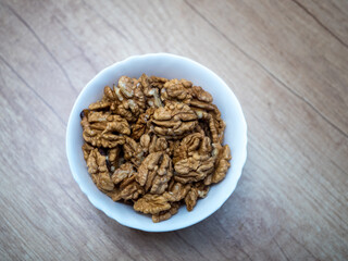 Top view of white bowl filled with raw walnut kernels on wooden table. Natural food ingredient rich in nutrients, suitable for healthy breakfast, baking cakes, desserts and home cooking.
