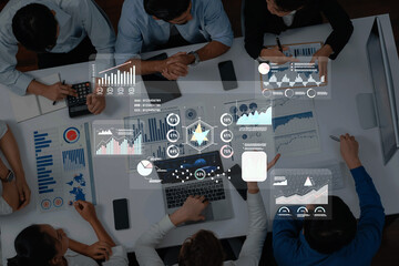 A top view of a diverse business team engaged in collaborative analysis, utilizing digital tools...