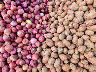 Fresh red onions and potatoes piled together for sale at a farm market stall