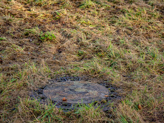 Verschmutzter Schachtdeckel auf einer Wiese
