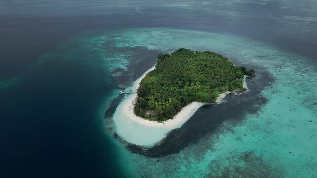 Aerial slow orbit drone shot over a tropical island surrounded by coral reef in the Maluku region