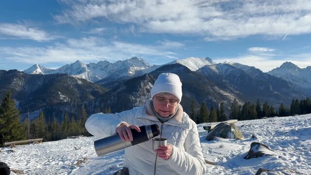 Portrait of a woman with thermos drinking hot beverage on the winter snowy mountains background